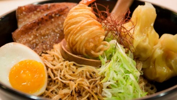 Foto jarak dekat, semangkuk mi telur kenyal, babi panggang, pangsit dan udang bungkus kentang, dilengkapi dengan telur rebus matang dari A Noodle Story