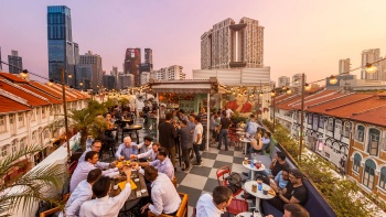 Para tamu di Potato Head Singapura, sedang makan, minum, dan bercakap-cakap saat matahari terbenam
