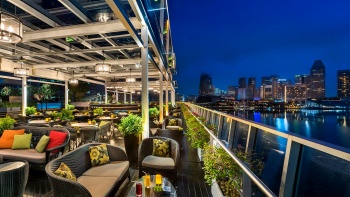 Saksikan bagian dalam bar Lantern yang berlatar tepi perairan Marina Bay dan cakrawala langit Singapura