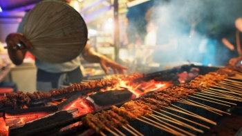 Foto jarak dekat seorang pria membakar sate di Satay by the Bay