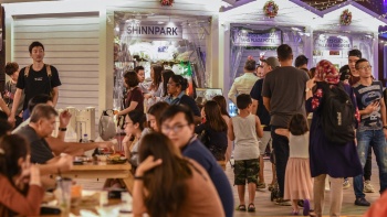 Orang mengantre di stan makanan dan bersantap di meja di Christmas Village.