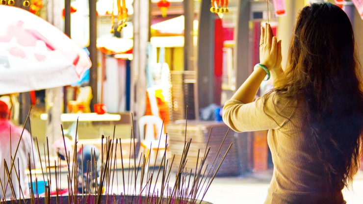 Foto seorang wanita tampak belakang yang sedang berdoa di depan tempat hio di kuil umat Buddha