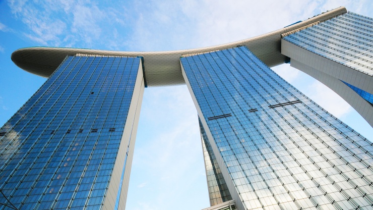 Foto fasad Marina Bay Sands<sup>®</sup> nan cantik diambil dari bawah mengarah ke langit biru nan menawan 