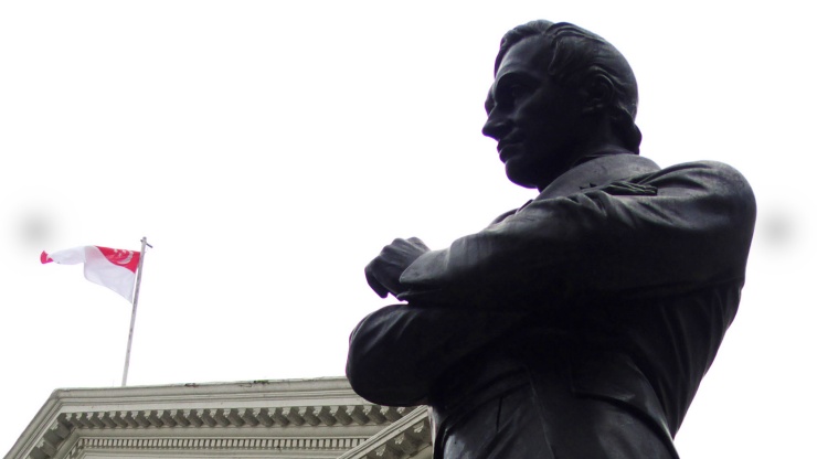 Patung tembaga Stamford Raffles dengan bendera Singapura berkibar di belakangnya