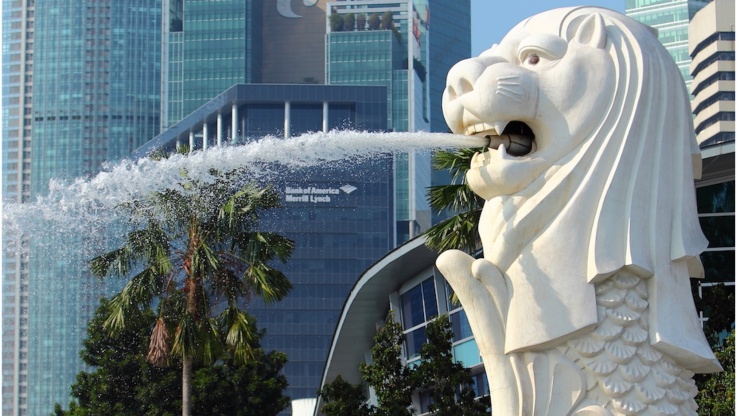 Gambar vertikal Merlion yang menyemburkan air saat siang, dengan cakrawala Singapura sebagai latarnya