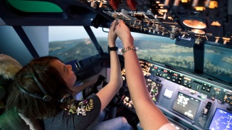 Pengambilan foto wanita di kursi pilot sembari memainkan sakelar panel kendali di Pengalaman Penerbangan Singapura.
