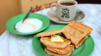 Potret jarak dekat roti panggang srikaya, telur setengah matang, dan secangkir kopi panas
