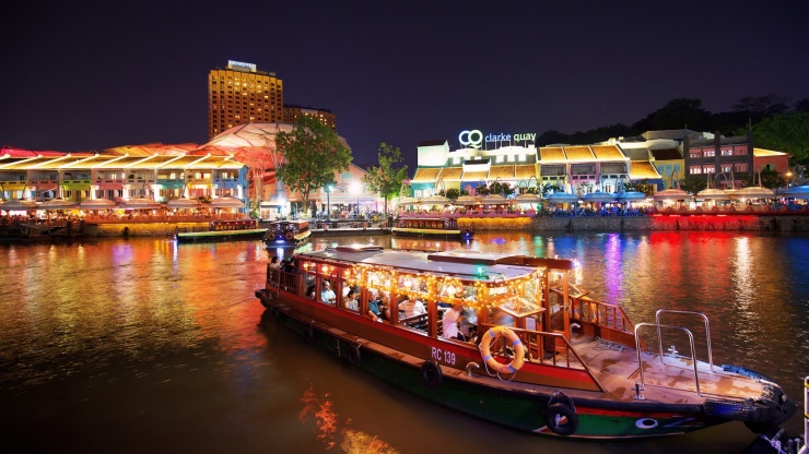 クラーク・キーの看板を背に、夜のシンガポール川を進むバムボート