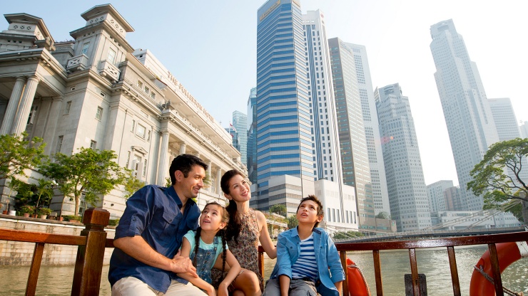 Young family looking up from a bumboat ride on the Singapore River, with Fullerton Hotel in the background.