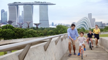 A happy family with children riding their bicycles at Marina Barrage with Marina Bay Sands in the background
