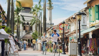 คู่รักขี่จักรยานไปตามตรอกซอกซอยโดยมี Sultan Mosque เป็นฉากหลัง