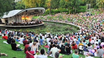 ผู้คนกำลังชมการแสดงที่ Shaw Foundation Symphony Stage (เวทีการแสดงดนตรีซิมโฟนี่ของมูลนิธิชอว์) ณ Singapore Botanic Gardens (สวนพฤกษศาสตร์สิงคโปร์)