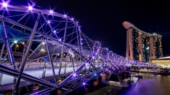 คุณจะตื่นตะลึงกับ The Helix สะพานรูปทรงคล้ายสายดีเอ็นเอในช่วงค่ำคืนและมี Marina Bay Sands® เป็นฉากหลัง 