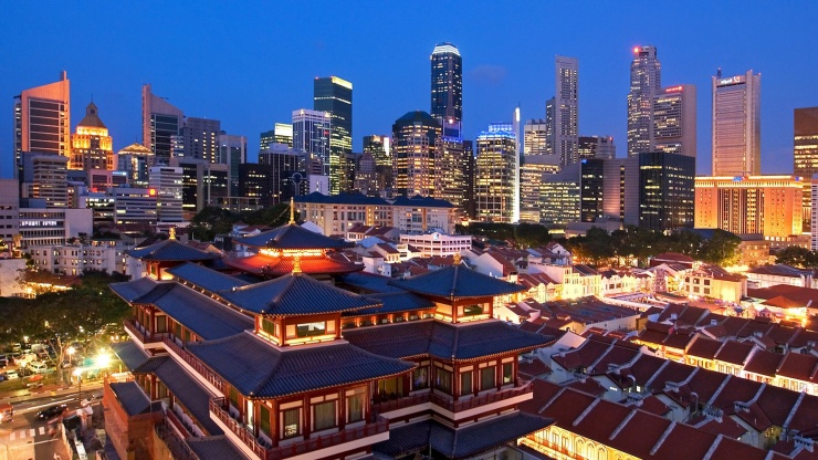 ภาพมุมสูงของย่าน Chinatown พร้อมด้วย Buddha Tooth Relic Temple ในยามค่ำคืน โดยมีตึกระฟ้าในย่านธุรกิจใจกลางเมืองเป็นฉากหลัง 