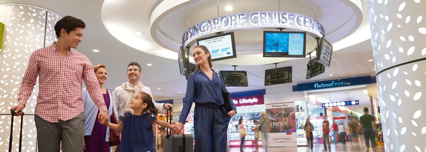 ครอบครัวที่มีสมาชิกห้าคนกำลังเดินข้ามล็อบบี้ของ Singapore Cruise Center (สิงคโปร์ ครูซ เซ็นเตอร์) พร้อมด้วยกระเป๋าสัมภาระ