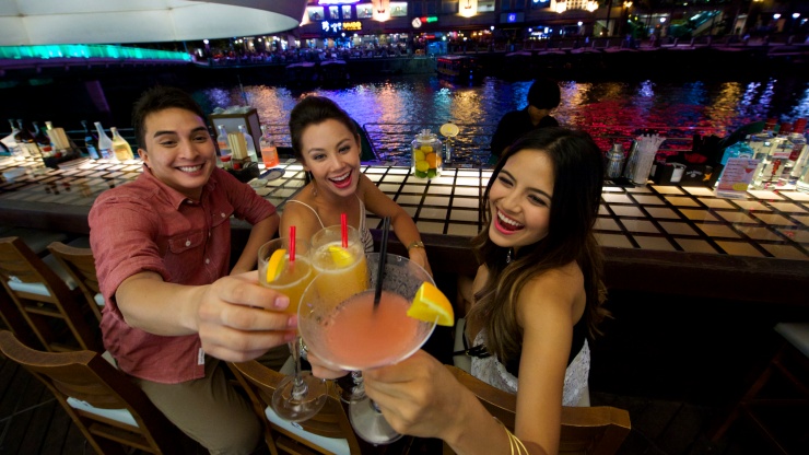 เพื่อน 3 คนกำลังเพลิดเพลินกับเครื่องดื่มในย่าน Clarke Quay