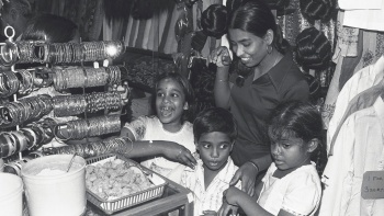 A black and white photo of a young Indian mum with her three young children at a textiles and jewellery store