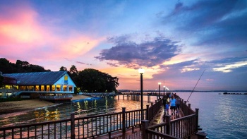 Hình chụp từ xa một gia đình tản bộ dọc theo Changi Boardwalk lúc hoàng hôn