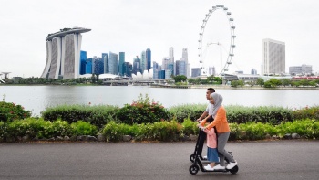 Một gia đình trên chiếc xe scooter chạy điện, phía xa là khung cảnh Marina Bay.